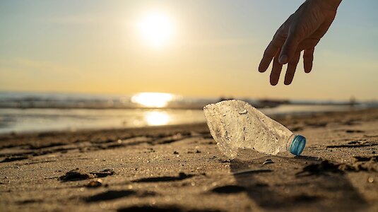 Person sammelt Plastikflasche am Strand auf